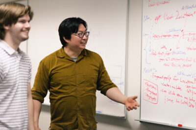 Louis Yu teaching in front of whiteboard. 